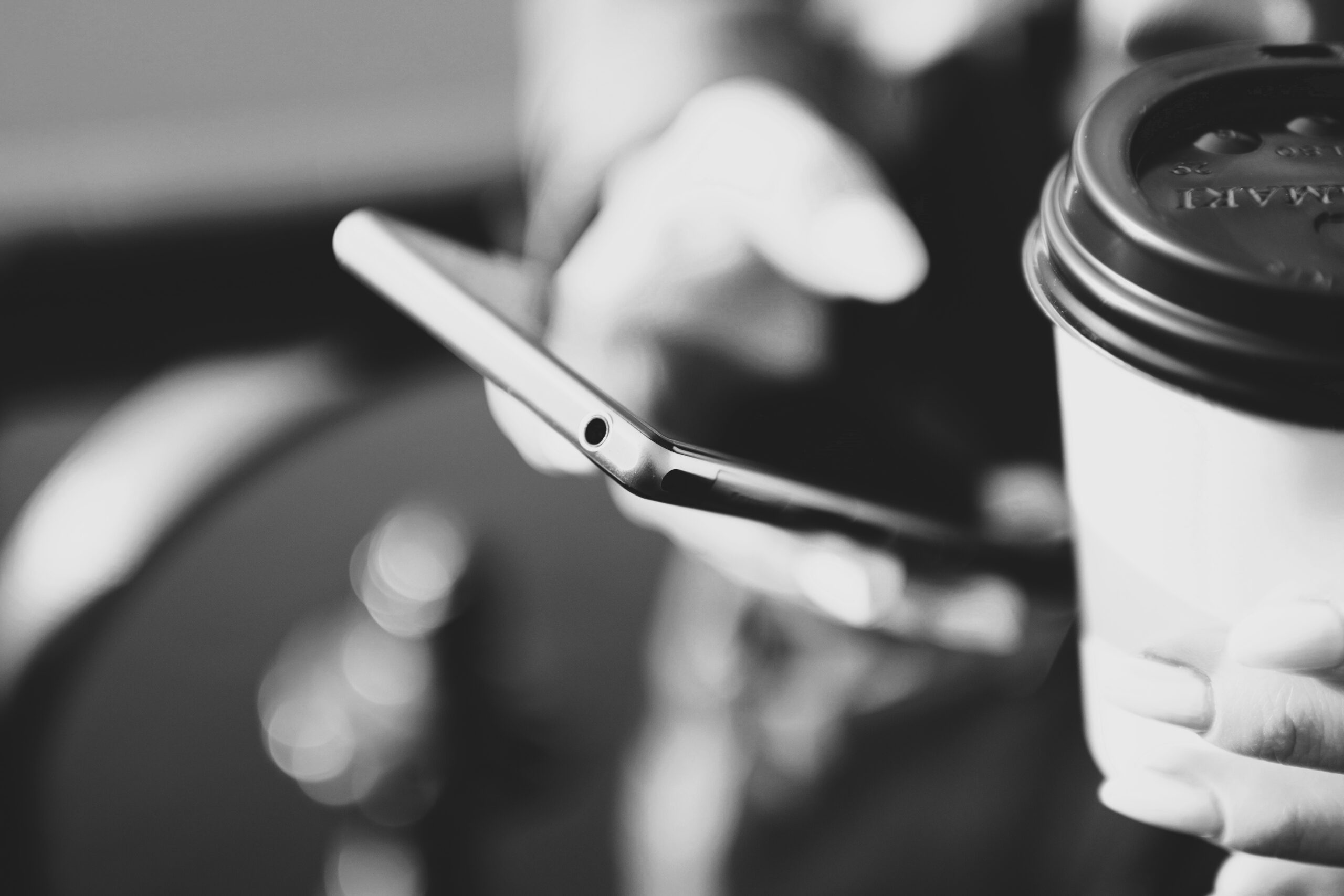 personne tenant son smartphone dans une main et un café dans l'autre